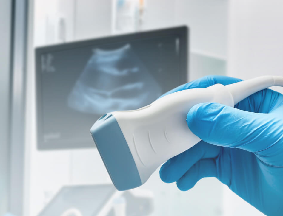 A gloved hand holds an ultrasound probe, with a blurry ultrasound image on a screen in the background, evoking a clinical and professional setting.