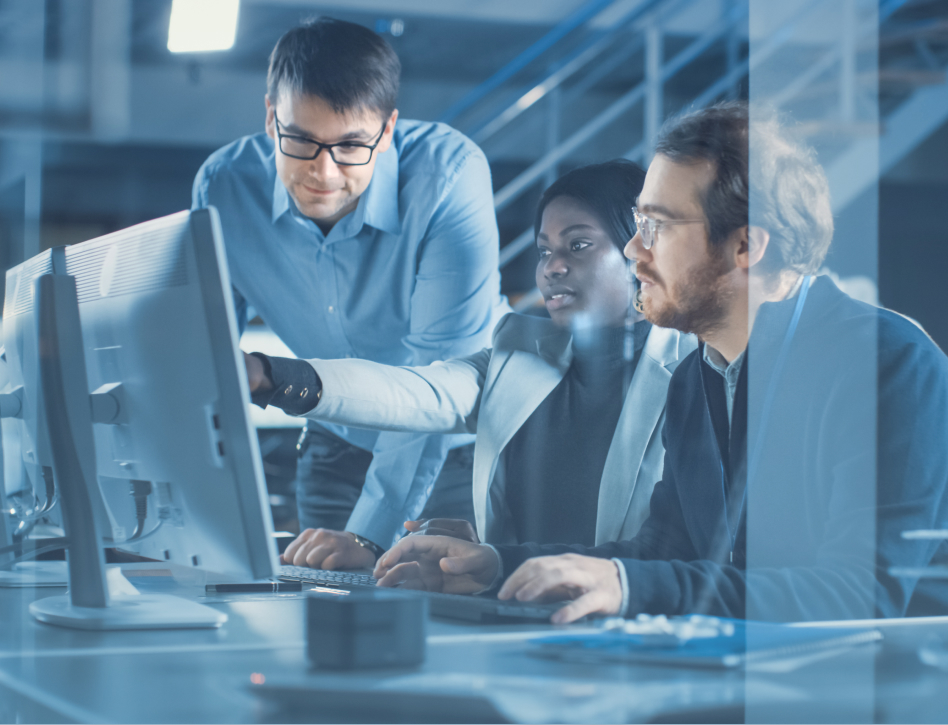 Three diverse coworkers collaborate at a computer in a modern office, reviewing information on-screen with focused, professional expressions.